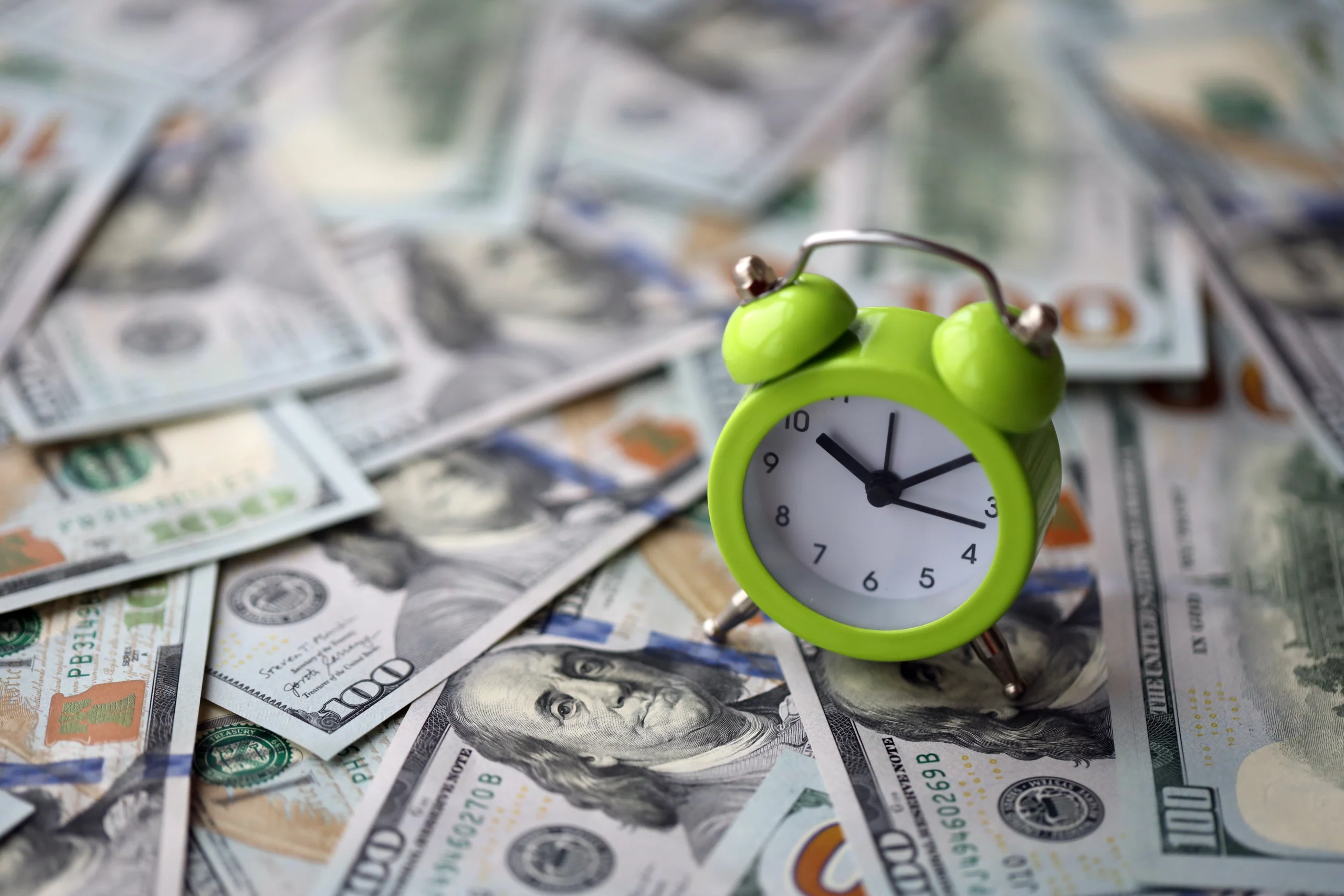 Green alarm clock on scattered hundred-dollar bills, symbolizing urgency around California wage and hour violations and unpaid wages.