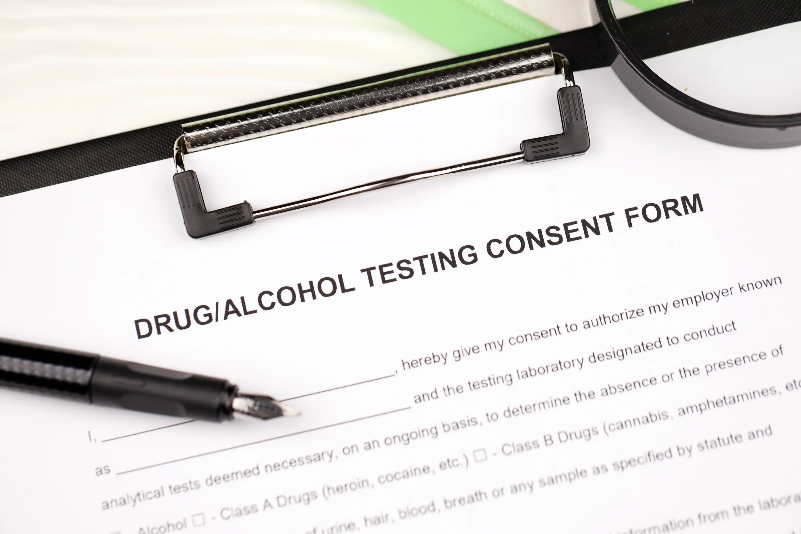 Drug and alcohol testing consent form with pen and magnifying glass illustrating workplace drug test wrongful termination legal blog