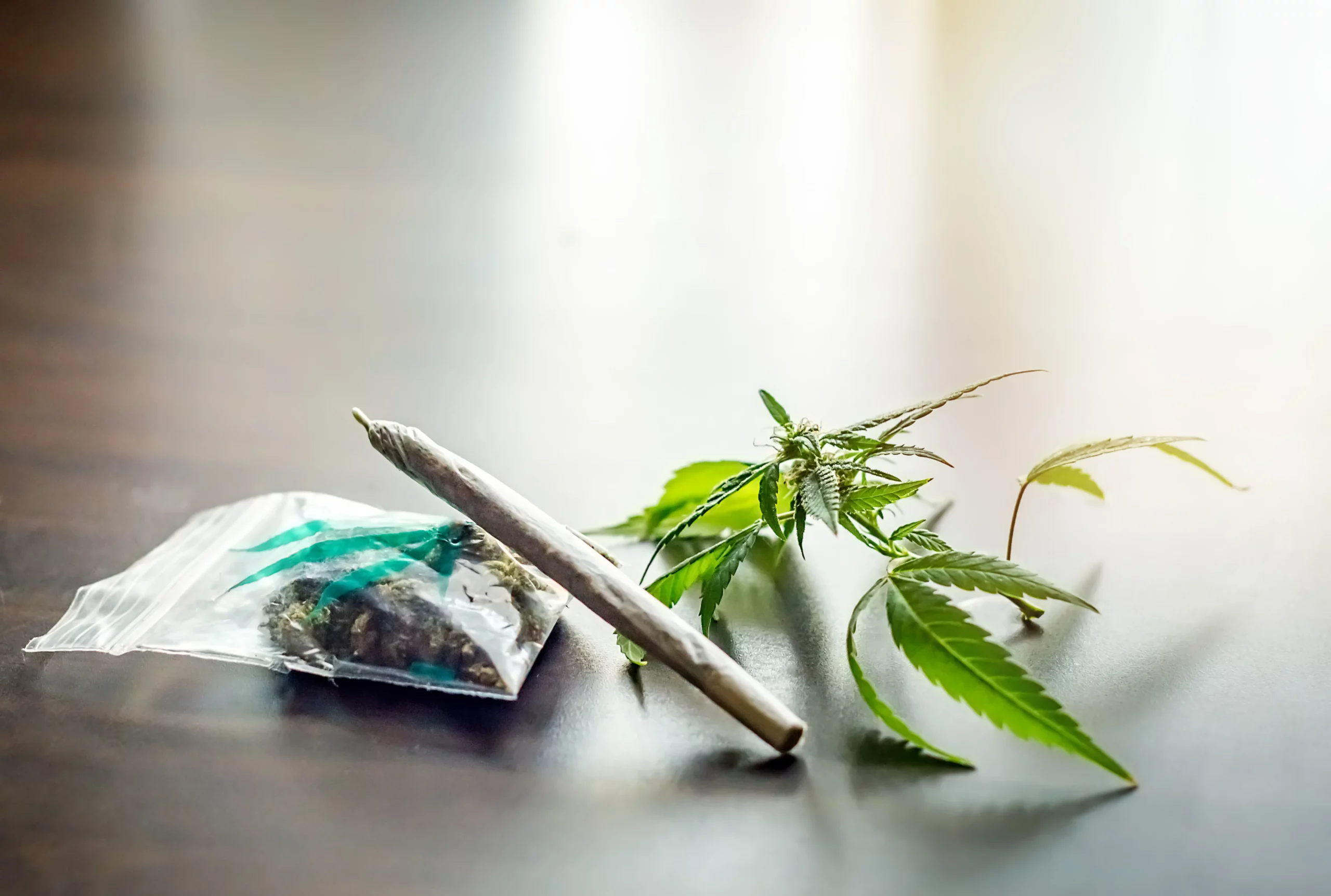 Rolled joint and cannabis leaves on wood table for California off-duty marijuana wrongful termination blog.