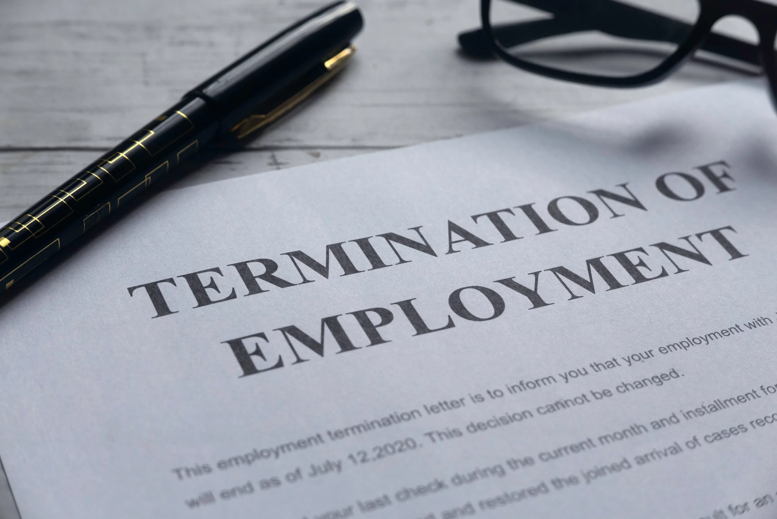 Close-up of a termination of employment letter on a desk with a pen and eyeglasses, illustrating wrongful termination versus at-will employment laws in California.